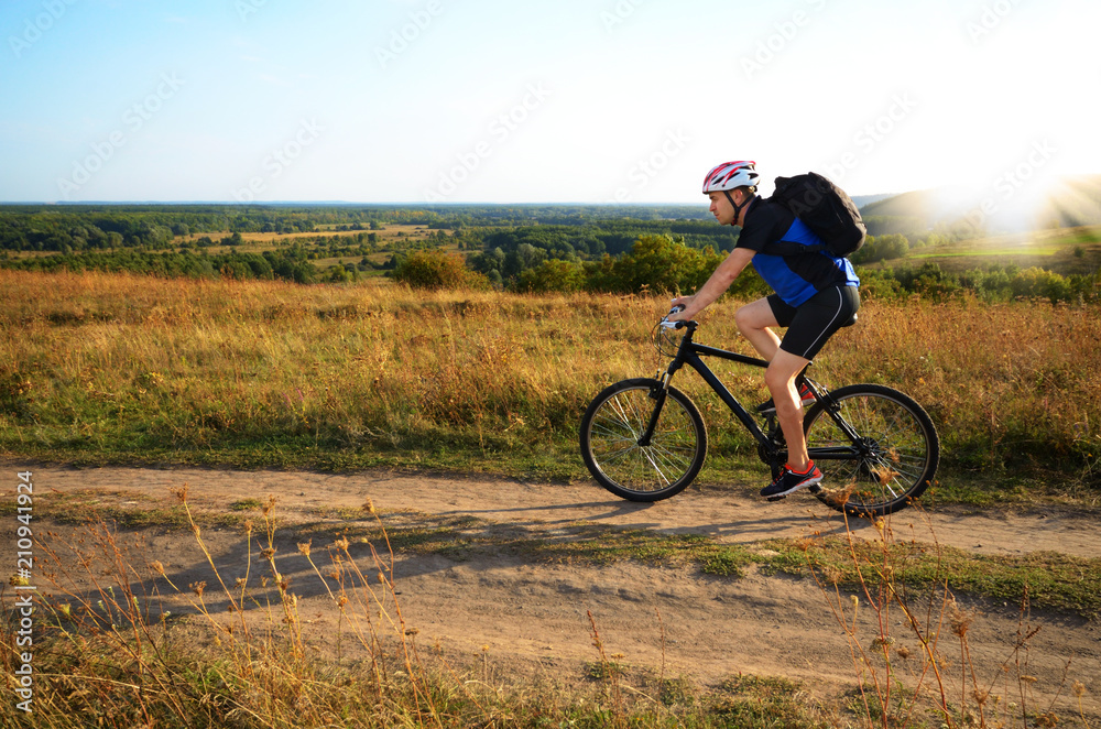 Male cyclist with backpack driving by rural dirt road outdoors