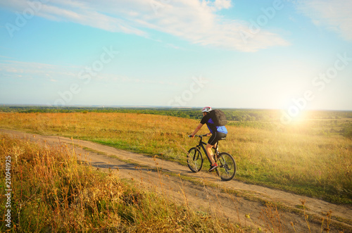 Male cyclist with backpack driving by rural dirt road outdoors