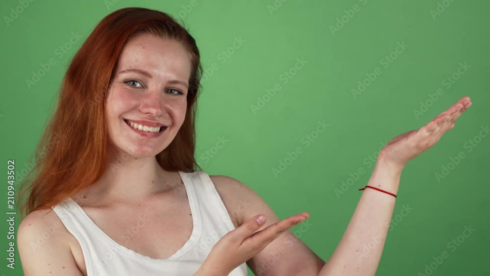 Studio portrait of a young attractive ginger haired female smiling to the camera joyfully holding copy space on the side on her hands. Beautiful woman presenting product. Advertising concept.