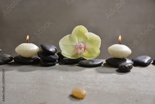 candle with pile of black stones and yellow orchid, herbal ball.towel on gray background