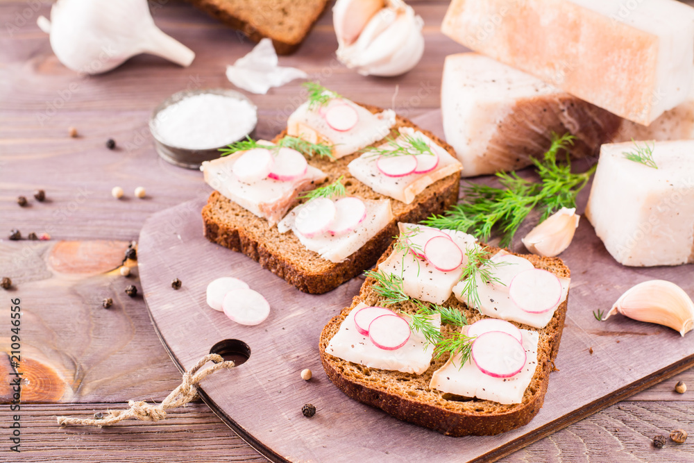 Sandwiches from rye bread, salted bacon, radish and dill on a cutting board on a wooden table Sandwiches from rye bread, salted bacon, radish and dill on a cutting board on a wooden table