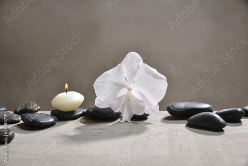 candle with pile of black stones and white orchid  on gray background