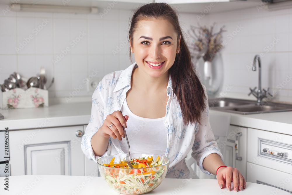 Healthy young woman eating salad on the kitchen