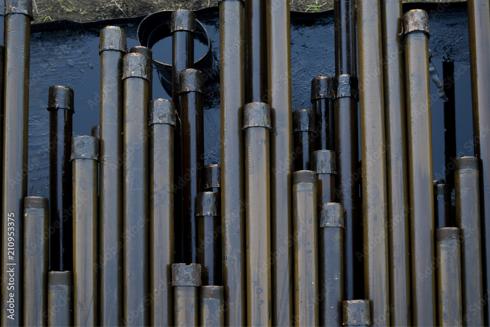 Oil Drill pipe. Rusty drill pipes were drilled in the well section. Downhole drilling rig. Laying the pipe on the deck. View of the shell of drill pipes laid in courtyard of the oil and gas warehouse. Oil Drill pipe. Rusty drill pipes were drilled in the well section. Downhole drilling rig. Laying the pipe on the deck. View of the shell of drill pipes laid in courtyard of the oil and gas warehouse.