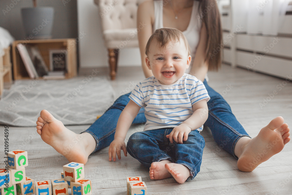 Young pretty mother playing with her little son. Cheerful family having fun indoors with little baby son Young pretty mother playing with her little son. Cheerful family having fun indoors with little baby son