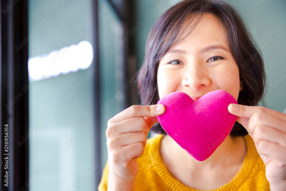 Young asian woman making air kiss to pink heart pillow. Love, care, health concept. Young asian woman making air kiss to pink heart pillow. Love, care, health concept.