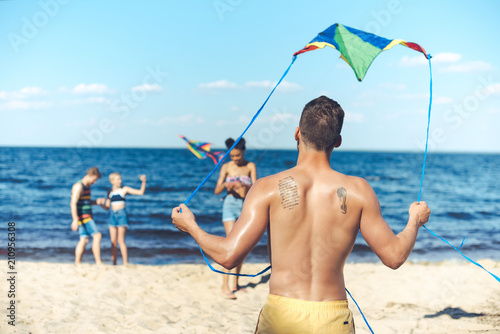 selective focus of interracial group of friends with kites having fun on sandy beach