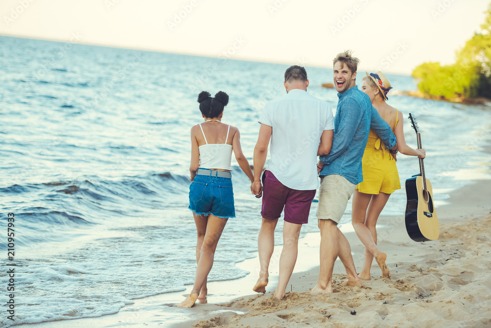 multiethnic group of friends with acoustic guitar walking together by sea