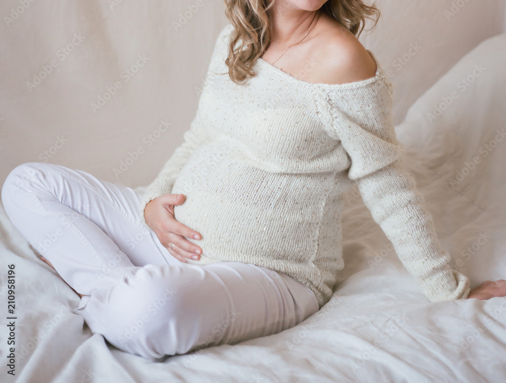 Pregnant girl sits on the bed with legs crossed Pregnant girl sits on the bed with legs crossed