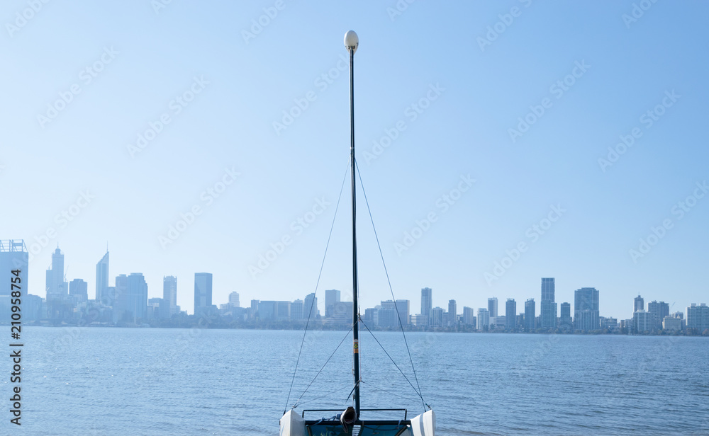 A sail boat on a river shore with Perth city skyline in the background