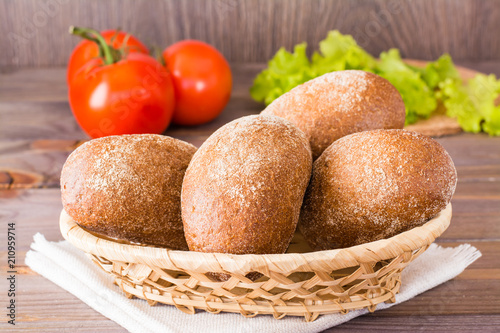 Fresh rye buns in a basket, salad and tomato on a wooden table
