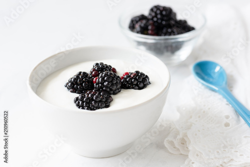 Greek yogurt with blackberries in white bowl on white background, closeup view