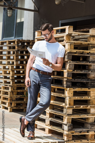 Fashionable confident businessman smoking cigar and reading report by wooden palettes