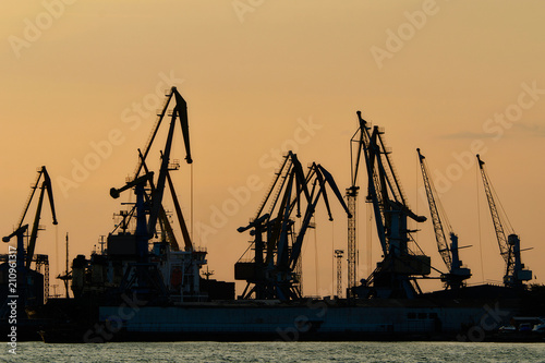 Silhouettes of port cargo cranes at sunset sky background