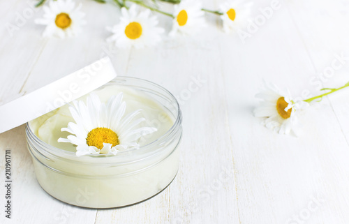 Opened plastic container with cream and chamomile flower on a light background. Herbal dermatology cosmetic hygienic cream Spa concept organic cosmetic Natural beauty product.