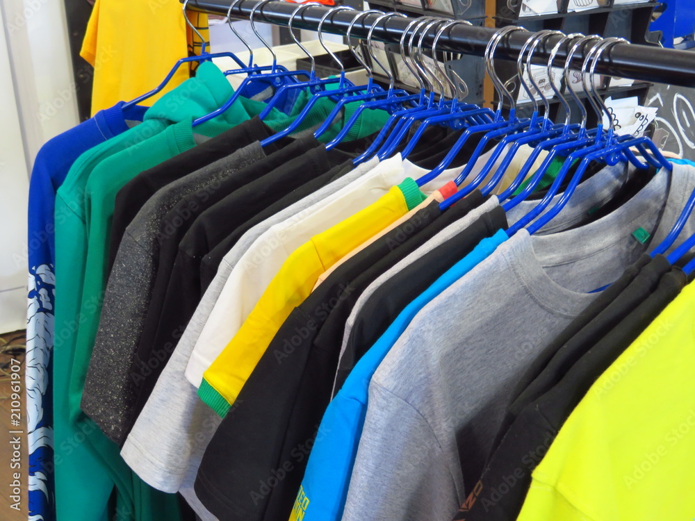 Obraz premium Clothes hanging on a hanger in the store. Choice of Women's t-shirts of different colors on metal hangers.