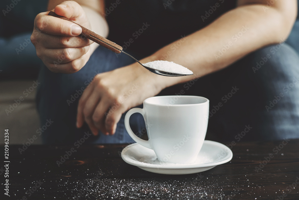 Sugar addiction, unhealthy lifestyle, weight gain, dietary, healthcare and medical concept. Cropped portrait of woman pouring sugar into coffee cup Sugar addiction, unhealthy lifestyle, weight gain, dietary, healthcare and medical concept. Cropped portrait of woman pouring sugar into coffee cup