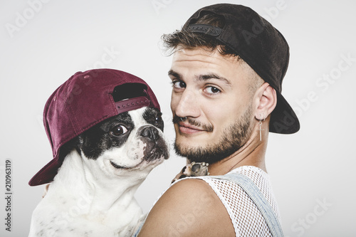 Hipster guy hugging his nice French Bulldog dog against neutral background