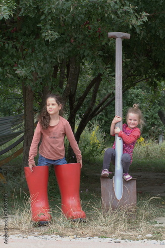 Sisters girls play in the garden in giant rubber boots, with a big shovel photo