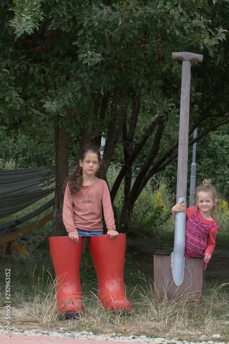 Sisters girls play in the garden in giant rubber boots, with a big shovel photo