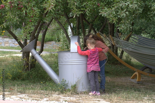 Sisters girls play in the garden with a big garden watering can