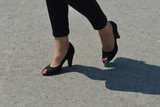 Woman's legs with red nails polished in black sandals walking on the street