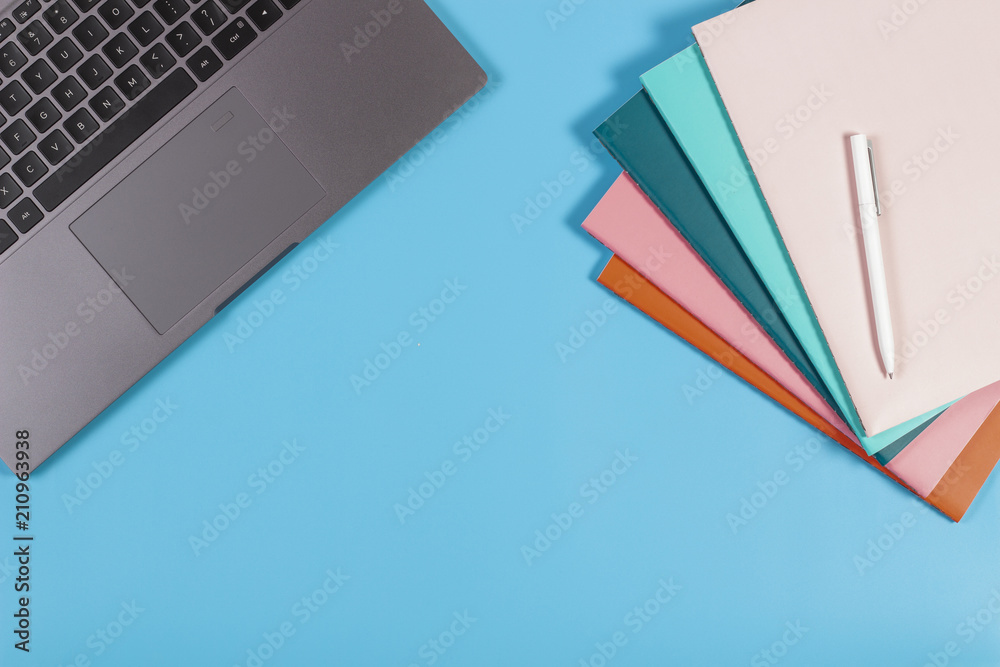 Workspace with laptop keyboard and colorful notebooks on blue background.