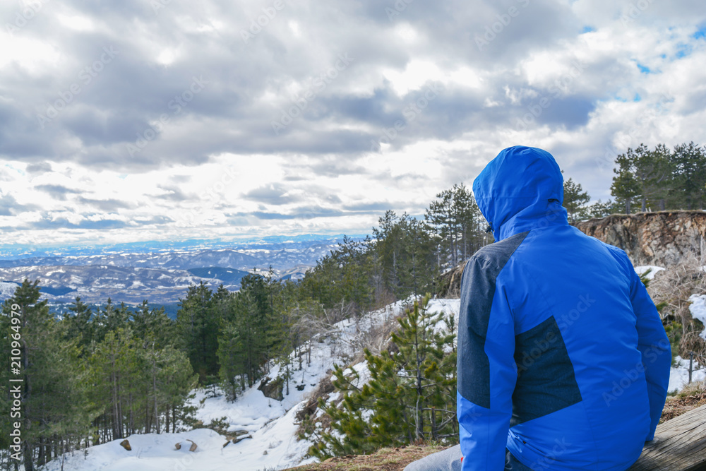 One hiking man with hood sitting on on view point and looking on valley One hiking man with hood sitting on on view point and looking on valley