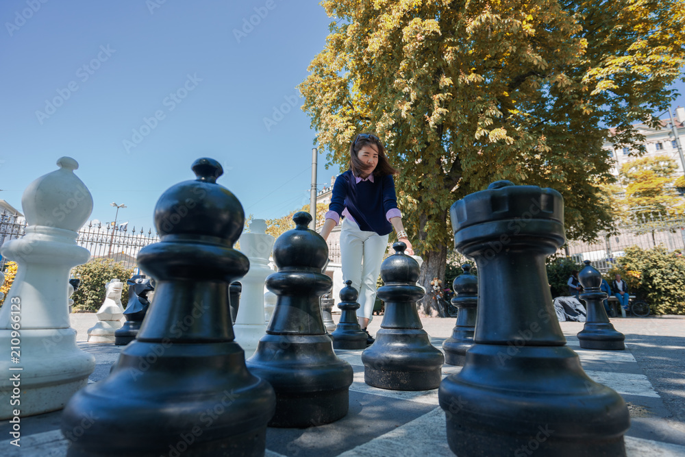 A business woman is thinking about strategy to win in the giant chess game in the garden.
