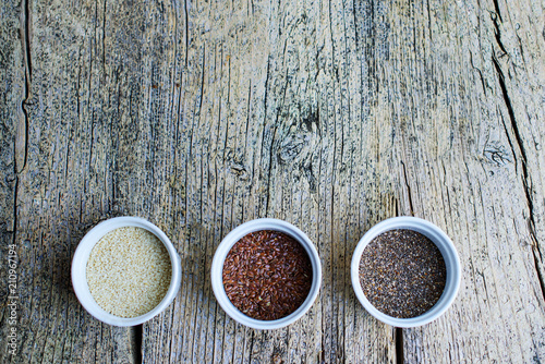 Three superfoods chia, flax and sesame seeds in white pals on a wooden background