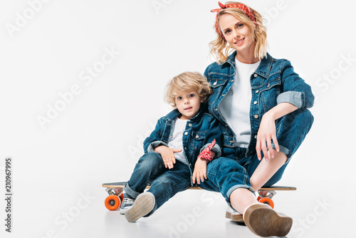mother and son sitting on skateboard and looking at camera on white