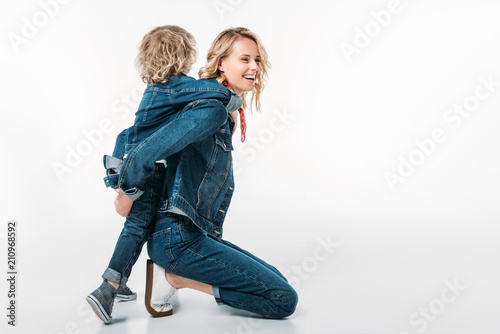 Φωτογραφία side view of happy mother giving piggyback to son on white