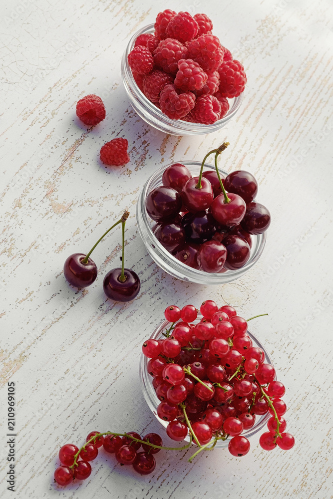 Fresh raspberries, red currants and cherries in glass bowls. vertical Fresh raspberries, red currants and cherries in glass bowls. vertical