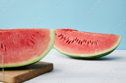 close up view of arranged watermelon slices on cutting board and white surface on blue backdrop