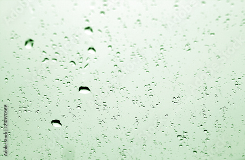 Rain drops on car window in green tone with blur effect.