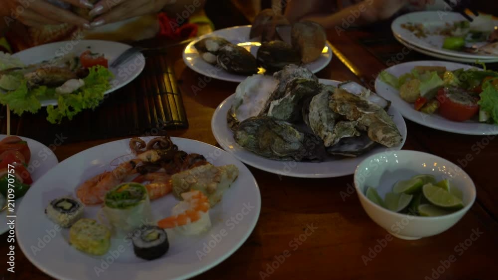 Table with plates of seafood. Women's hands take the oyster Table with plates of seafood. Women's hands take the oyster