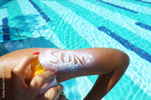 Sun text on sunscreen applied with spray on woman arm at poolside
