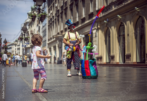 Little girl watching clown at the pedestrian street in the city