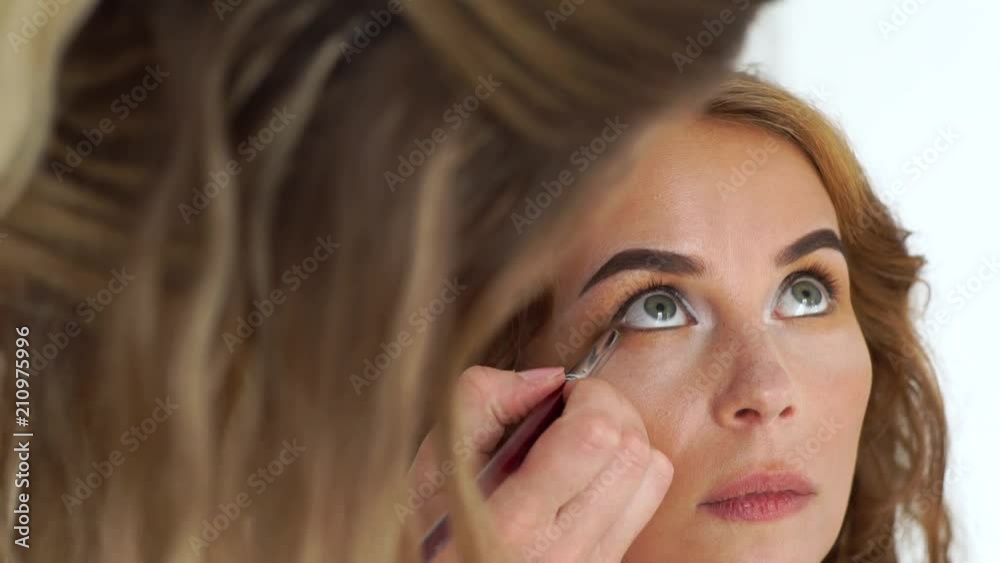 Make up artist working with beauty model and doing evening makeup eyes with cosmetic brush. Professional woman make up in beauty studio. Style and fashion concept. Make up artist working with beauty model and doing evening makeup eyes with cosmetic brush. Professional woman make up in beauty studio. Style and fashion concept.