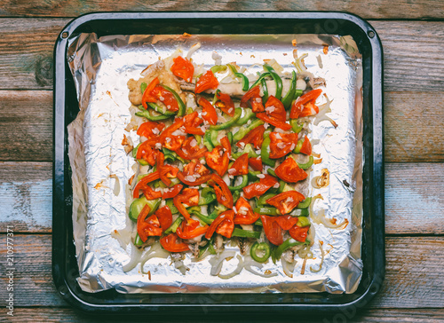 fish blue whiting baked with vegetables, tomatoes, bell pepper and onion on a baking sheet, top view close-up photo