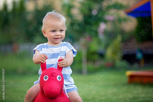 Little toddler child, boy, riding plastic horse toy in backyard photo