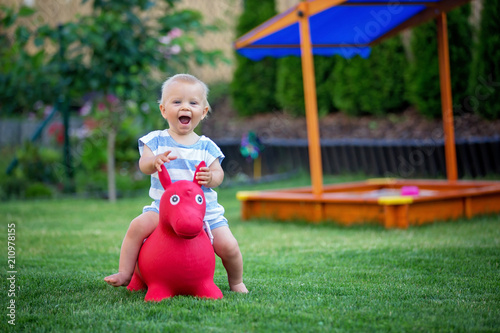 Little toddler child, boy, riding plastic horse toy in backyard photo