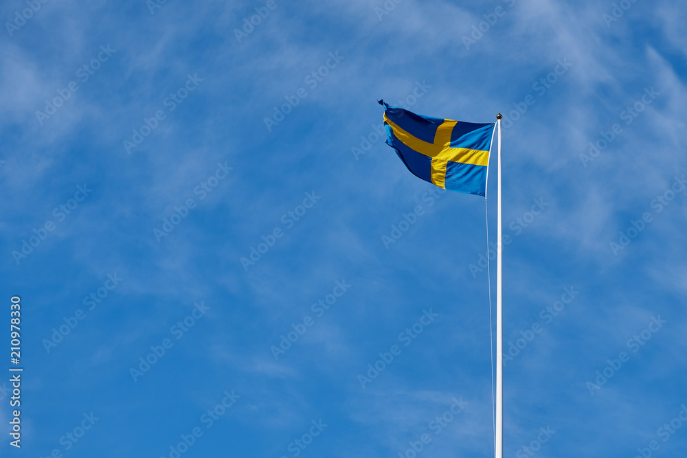 Flag of Sweden against a blue cloudy sky on a background. Copy space for text. Flag of Sweden against a blue cloudy sky on a background. Copy space for text.