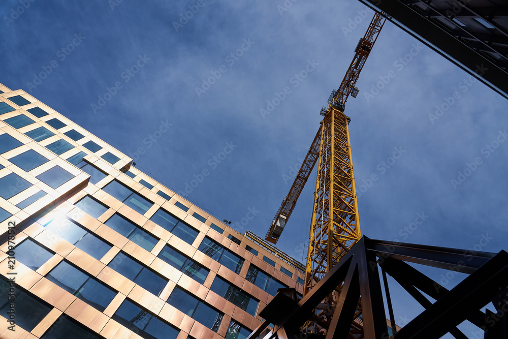 Yellow construction crane in the sunlight between houses against a blue cloudy sky. Yellow construction crane in the sunlight between houses against a blue cloudy sky.