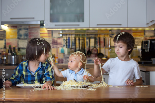 Little baby boy, toddler child and his older brothers, eating spaghetti for lunch and making a mess
