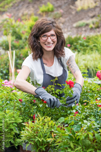 Fröhlich lächelnde Gärtnerin beim schneiden der Rosenpflanzen