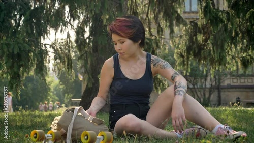 Asian young women with tattoo standing from grass and going to university, holding backpack and skateboard photo