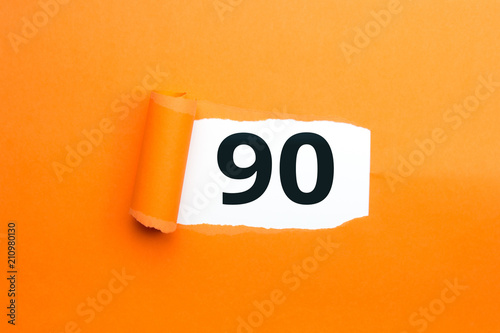 Zahl neunzig - 90 verdeckt unter aufgerissenem orangen Papier photo