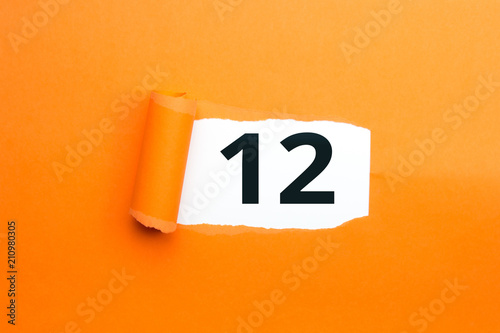 Zahl zwölf - 12 verdeckt unter aufgerissenem orangen Papier