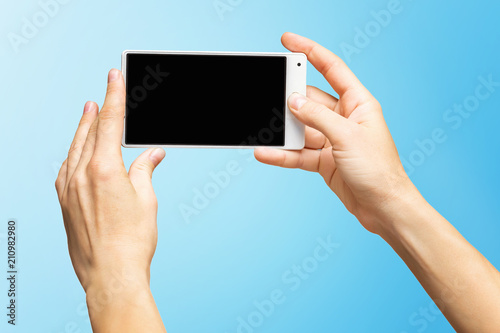 Mockup of female hands holding white frameless cellphone with black screen and making selfie at isolated blue background.